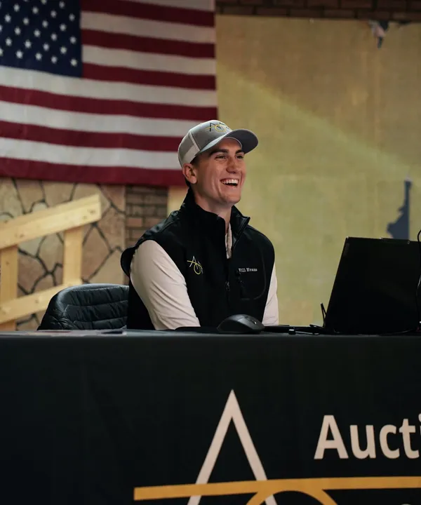 Man smiling beside American flag, sitting at desk.